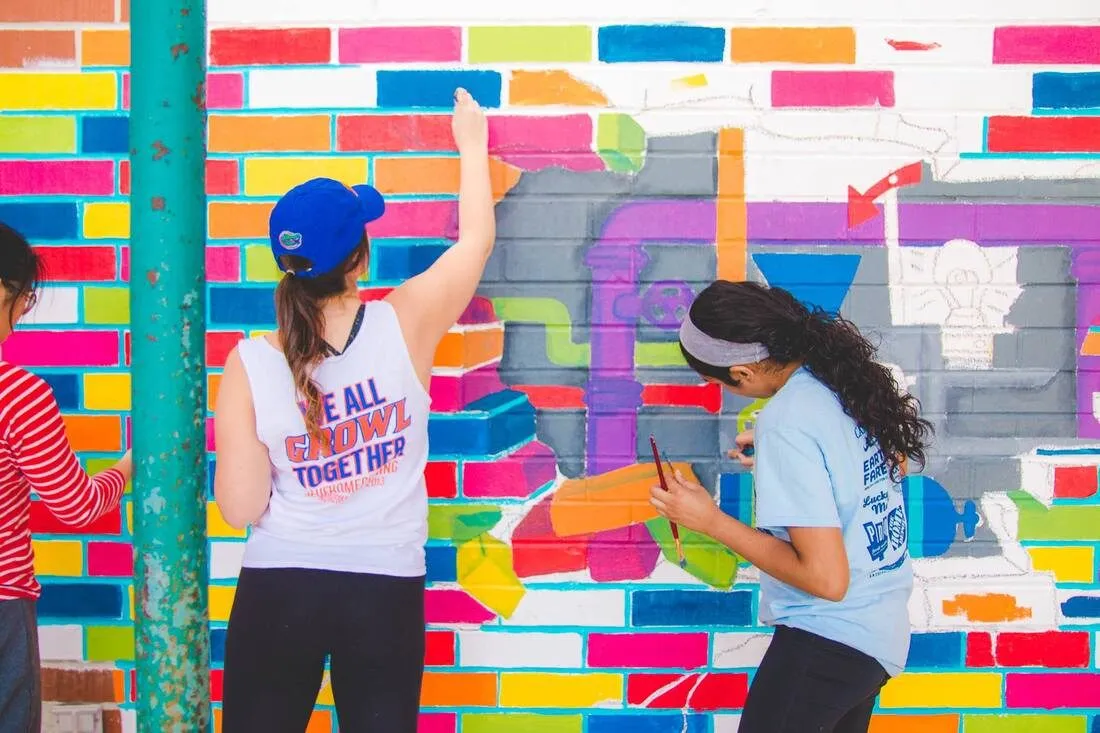 Two volunteers painting a wall of bright multicoloured bricks