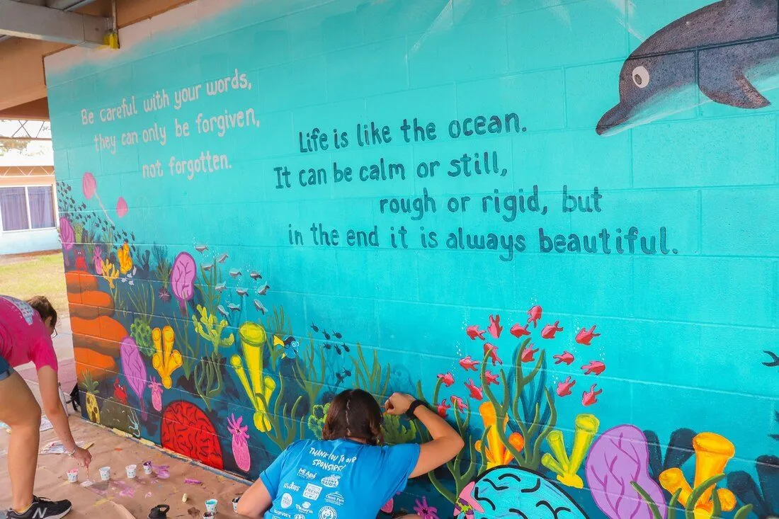 An ocean mural covering a school wall, with coral, fish and a dolphin painted around a hand-lettered quotation