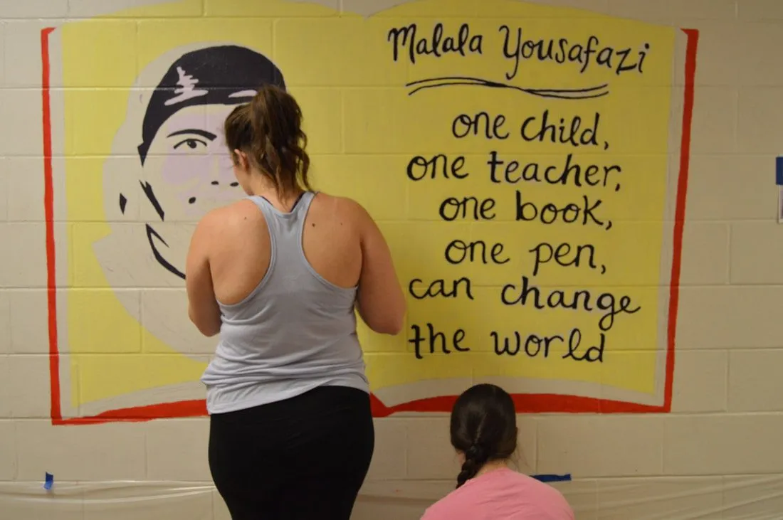 A volunteer painting a portrait of Malala Yousafzai beside her hand-lettered quotation