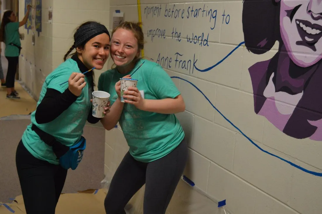 Two volunteers beside the finished Anne Frank mural and its hand-lettered quotation