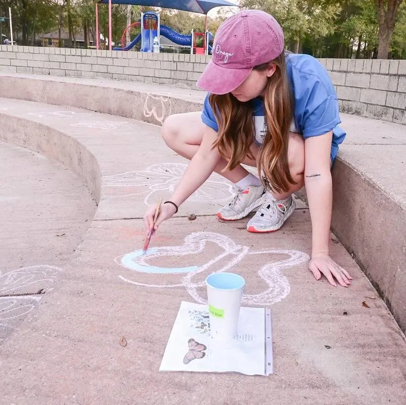 A volunteer painting a chalk-outlined butterfly onto the amphitheater steps