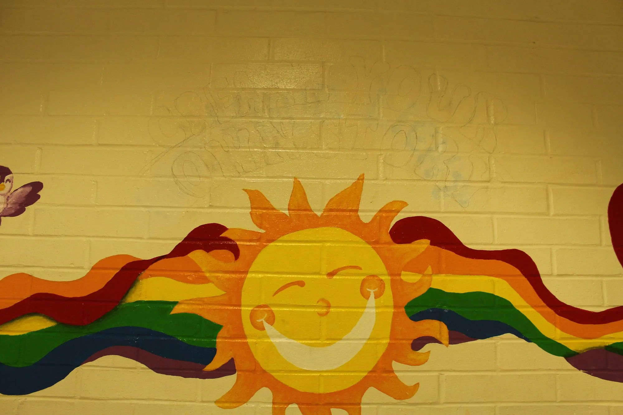 A smiling sun with a rainbow trailing from it, painted along a corridor wall