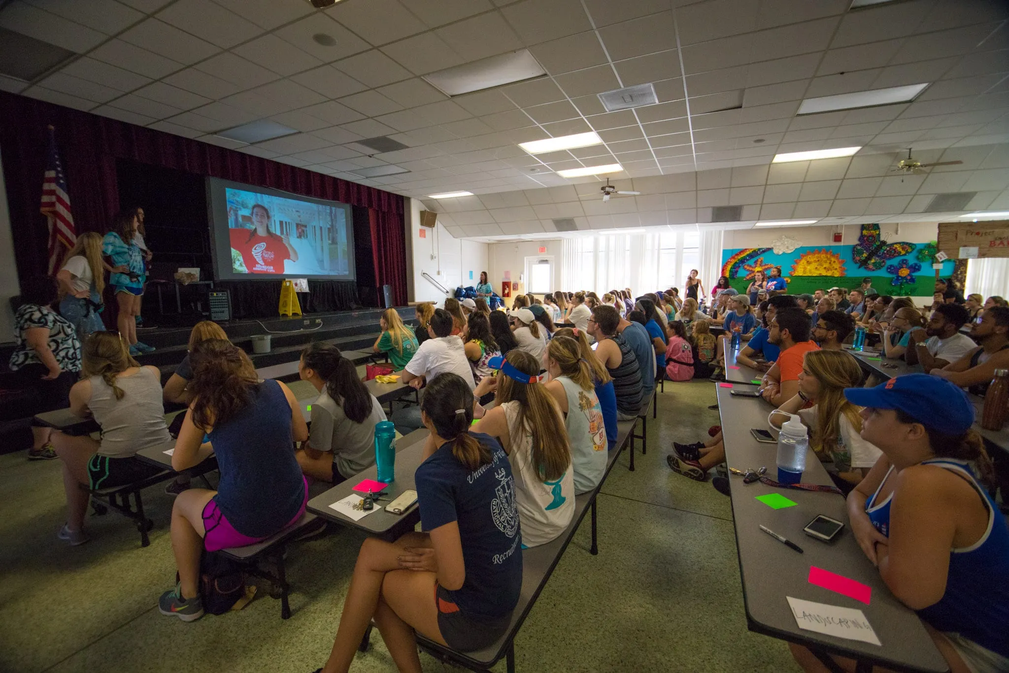 A room full of volunteers listening to a briefing in a school cafeteria