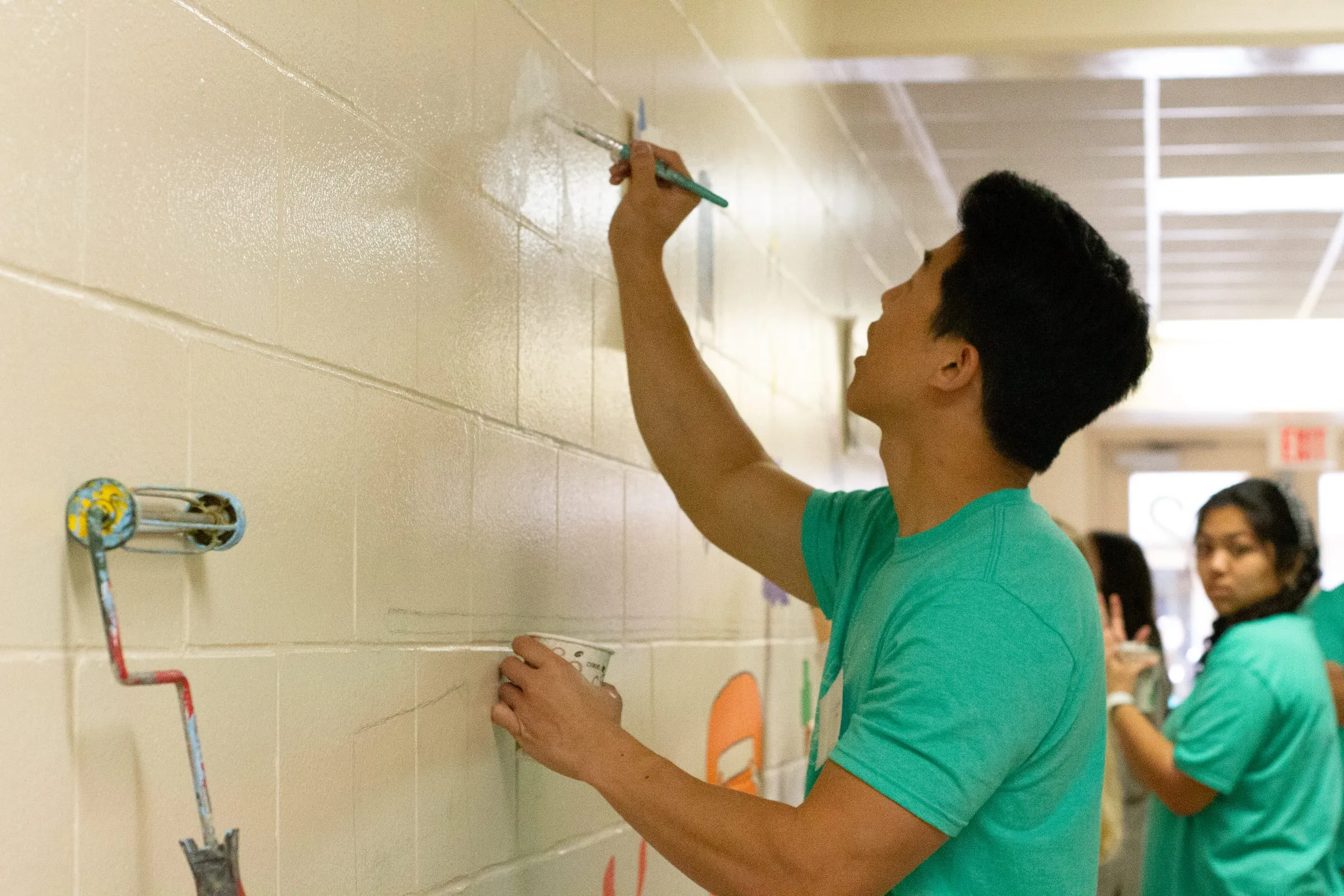 A volunteer painting a mural in a school hallway
